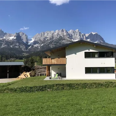 A modern house in a picturesque mountain landscape. Impressive mountains and a clear blue sky can be seen in the background.