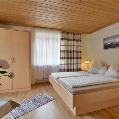Ein gemütliches Schlafzimmer mit Holzdecke und zwei Betten. Geplant mit einem Kleiderschrank und einem Blumenarrangement auf dem Tisch.