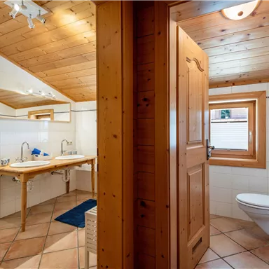Ein modernes Badezimmer mit Holzverkleidung und zwei Waschbecken. Es gibt ein Fenster und eine klare, helle Atmosphäre.