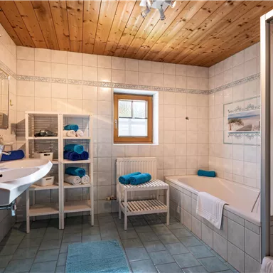Ein modernes Badezimmer mit hellen Fliesen und Holzdecke. Die Ausstattung umfasst ein Waschbecken, eine Badewanne und eine Dusche.