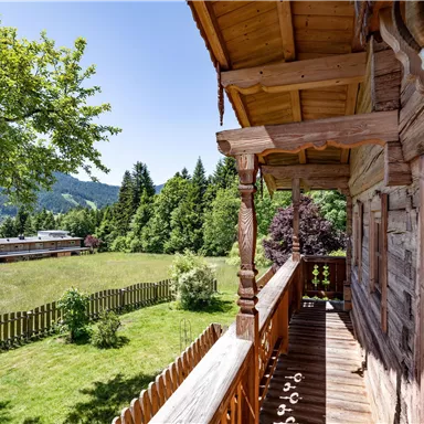 Ein schöner Blick von einem Balkon auf eine grüne Wiese und Bäume. Die Berglandschaft im Hintergrund sorgt für eine entspannte Atmosphäre.
