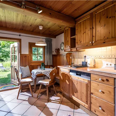 Eine gemütliche Holz-Küche mit einem Esstisch und Stühlen. Ein Fenster öffnet sich zu einem grünen Garten.