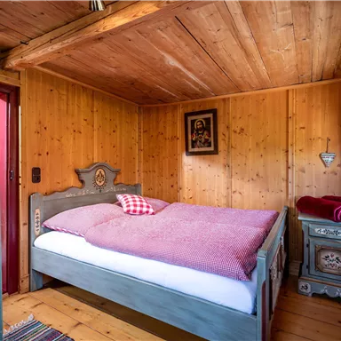 Ein gemütliches Schlafzimmer mit holzverkleideten Wänden und einem großen Bett. Die Einrichtung ist rustikal mit einem traditionellen Nachttisch und dekorativen Elementen.