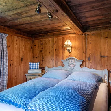 Ein gemütliches Schlafzimmer mit Holzverkleidung und blauen Bettdecken. Die Einrichtung ist rustikal mit Fenster, Gardinen und dekorativen Kissen.