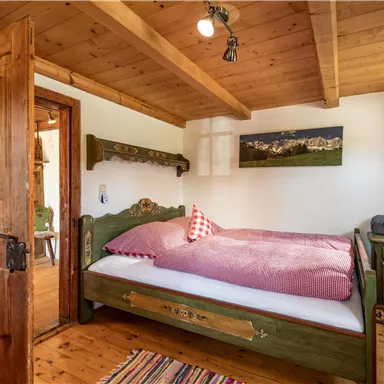 Ein gemütliches Schlafzimmer mit einem Holzbett und roter Bettwäsche. Das Zimmer hat Holzvertäfelungen und ein Fenster mit Vorhängen.