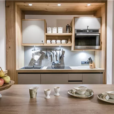 Eine moderne Küche mit Holzregalen und Edelstahlgeräten. Auf dem Tisch stehen Obst und Geschirr in eleganten Designs.