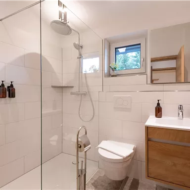 Ein modernes Badezimmer mit einer Dusche und einem Waschbecken aus Holz. Große Fliesen und ein Fenster sorgen für eine helle Atmosphäre.