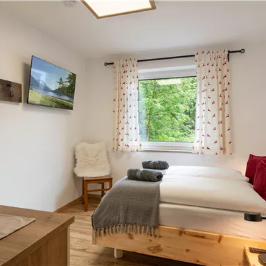 Ein gemütliches Schlafzimmer mit zwei Betten und einem großen Fenster. Die Einrichtung ist hell und freundlich, mit Pflanzen und dekorativen Elementen.