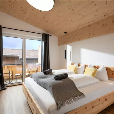 Ein gemütliches Schlafzimmer mit Holzmöbeln und einem großen Fenster. Die Dekoration ist einfach und modern, mit einem Balkon im Hintergrund.
