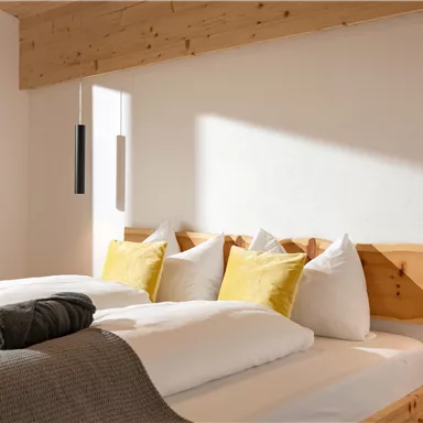Ein gemütliches Schlafzimmer mit einem Doppelbett und gelben Kissen. Sanftes Licht fällt auf die Holzwände und die moderne Dekoration.