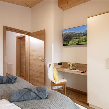 Ein modernes Schlafzimmer mit zwei Einzelbetten und einem Schreibtisch. An der Wand hängt ein Fernseher und es gibt eine Tür zu einem weiteren Raum.