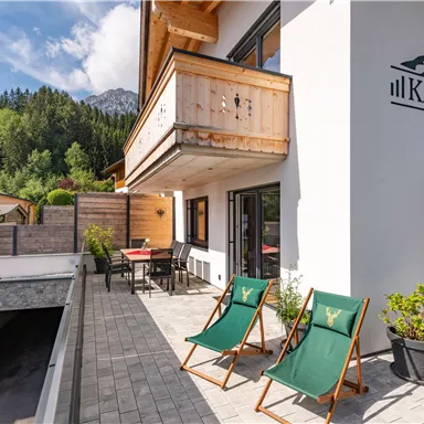 Eine moderne Chalet-Terrasse mit zwei Liegestühlen und Blick auf eine grüne Landschaft. Der Bereich ist einladend und sonnig, ideal zum Entspannen.