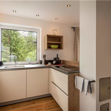 Eine moderne Küche mit hellen Schränken und einem großen Fenster. Der Raum hat eine warme Atmosphäre und Blick auf den Garten.