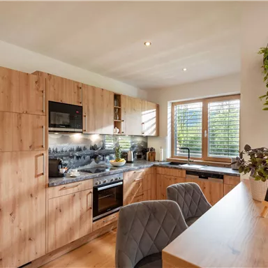 A modern kitchen with wooden shelves and appliances. The room is bright and inviting, with a small chalkboard that says "Welcome!"