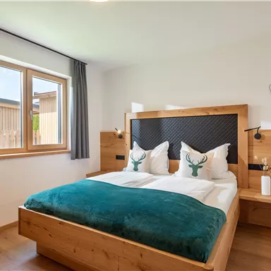A cozy bedroom with a large bed and wooden details. The room has a window with a view outside and decorative pillows.