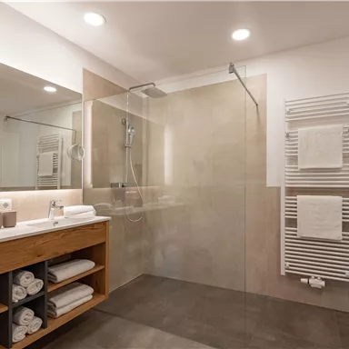 A modern bathroom with a transparent shower and a striking sink area. Towels are neatly stacked and the walls are in neutral tones.