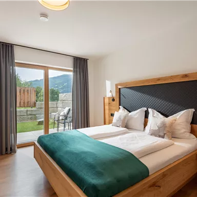 A modern bedroom with a double bed and a cozy decor. Large windows provide a view of the garden.