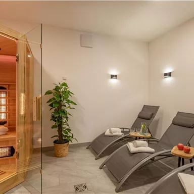 A relaxing wellness area with loungers and a sauna. The room is modern and brightly designed, with a plant and fresh apples on the table.