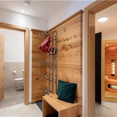A modern entrance with wooden cladding and a seating area. On the right side, there is a sauna, while in the background, a door to a bathroom is visible.