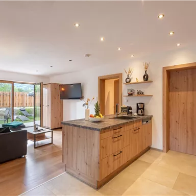 A modern kitchen with wooden cabinets and an island. The space is bright and friendly with access to a garden.