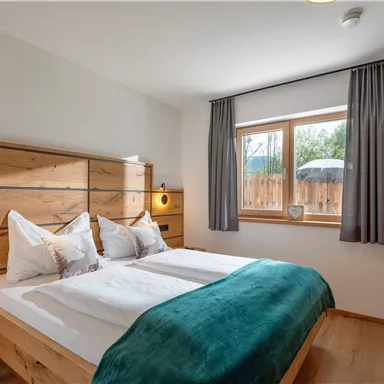 A cozy bedroom with a double bed and modern wooden furniture. Large windows provide plenty of daylight and a view of the outdoors.