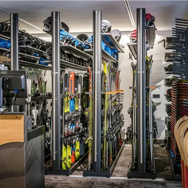 Ein Skiverleih mit mehreren Skiern und Snowboards, ordentlich aufgereiht. Im Vordergrund befindet sich der Verkaufstresen.