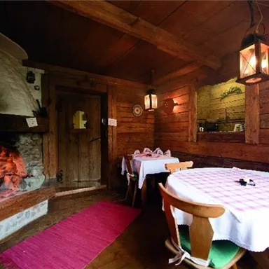 A cozy room with wooden decor and an open fireplace. Two tables are set with inviting tablecloths.