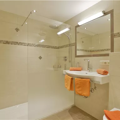Ein modernes Badezimmer mit einer Dusche und einem Waschbecken. Orangefarbene Handtücher verleihen dem Raum eine frische Note.