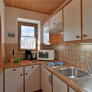 Eine helle Küche mit Holzdecke und modernen Geräten. Der Raum ist gut ausgestattet mit Spüle, Mikrowelle und einem Fenster, das viel Tageslicht hereinlässt.