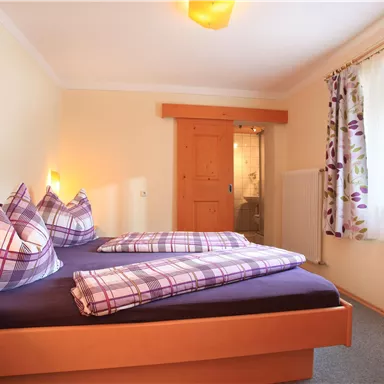 Ein gemütliches Schlafzimmer mit einem Doppelbett und karierten Kissen. Die Wände sind in sanften Farben gehalten, und ein Fenster sorgt für viel Tageslicht.