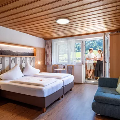 A cozy hotel room with a wooden ceiling and two beds. A couple stands in front of the balcony door and enjoys the view.