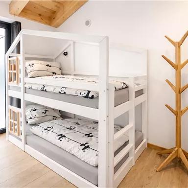 Ein modernes Kinderzimmer mit einem Etagenbett und weißen Bettwäsche, die mit Pandas bedruckt ist. An der Wand steht ein Holzkleiderständer und es gibt ein Fenster mit einem dekorativen Stern.
