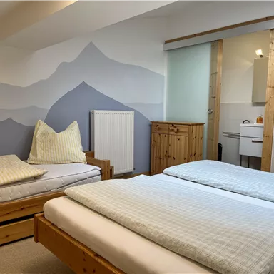 Ein gemütliches Schlafzimmer mit zwei Einzelbetten und einer modernen Einrichtung. Die Wände sind in sanften Farben mit einem Bergmotiv gestaltet.