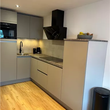 A modern kitchen with gray cabinets and a wooden floor. It is well-equipped with a stove, a sink, and a small table.