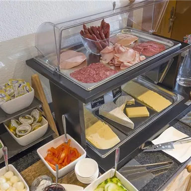 A rich breakfast buffet with various types of sausages and cheeses. Also included are small bowls of vegetables, jam, and sauces.