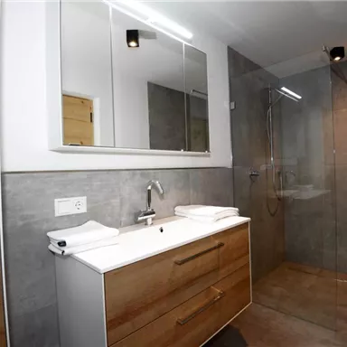 A modern bathroom with a large shower and a stylish sink. The walls are in neutral gray tones.