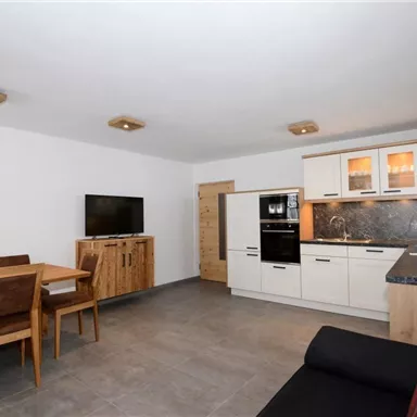 A modern kitchen with a dining area in a bright room. The decor is simple and functional with wooden and black accents.