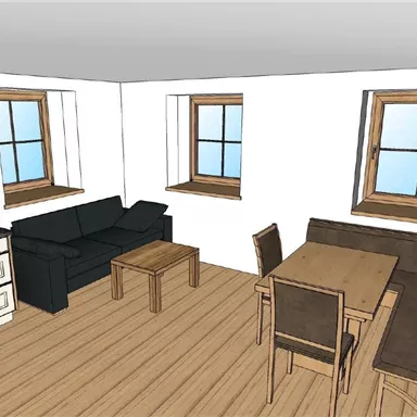 A simple living room with a black sofa, a table, and chairs. It has two windows that let in a lot of light.