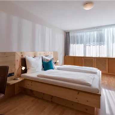 A bright room with two single beds and a large window. The furnishings are simple and made of light wood.