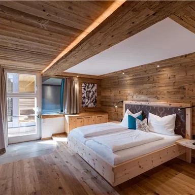 A modern bedroom with wooden paneling and large windows. The room is bright and inviting, equipped with a double bed and a television.