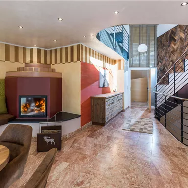 A modern living room with a cozy seating area and a fireplace. The staircase in the background leads to upper floors.