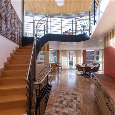 A modern staircase with wooden stairs and an elegant railing. The space has large windows that let in plenty of light, and a cozy seating area.