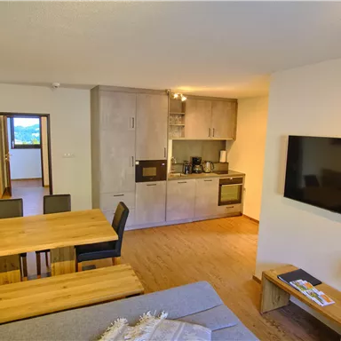 A modern apartment with an open living and kitchen area. The space features a dining table, a couch, and a television.
