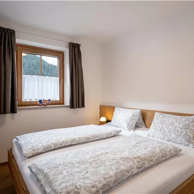 A cozy bedroom with a double bed and two nightstands. Large windows with curtains provide natural light.