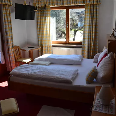 A cozy bedroom with a large bed and windows with blackout curtains. The room has a warm tone and includes a chair as well as a table.
