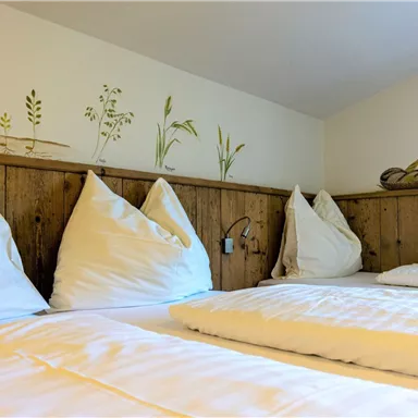 A cozy room with two beds and pillows. The walls are decorated with natural motifs.