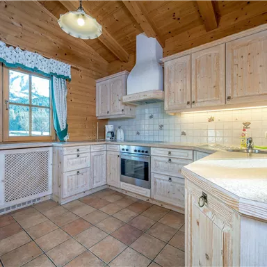 A cozy wooden kitchen with modern appliances. Large windows provide a view of nature.