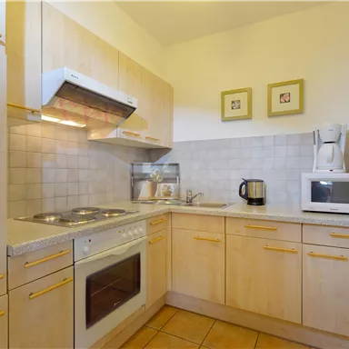 A modern kitchen with bright wood furniture and functional units. There is a stove, a microwave, and a kettle.