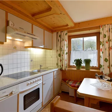 A cozy kitchen with wooden cladding and appliances such as a stove and a coffee machine. Plants are by the window, and a dining table invites you to linger.