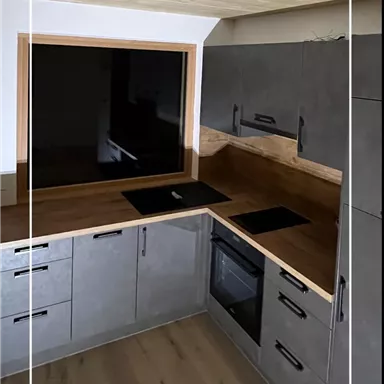 A modern kitchen with gray cabinets and a wooden countertop. The space has large windows and a bright atmosphere.